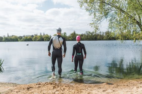 man-en-vrouw-in-wetsuits-lopend-naar-open-water.jpg