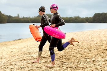 man-en-vrouw-rennend-naar-water-in-wetsuit-met-badmuts-en-zwemboei_002.jpg